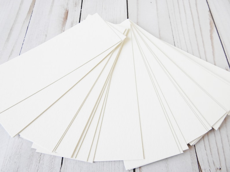 May include: A stack of blank white rectangular cards, fanned out on a white wooden surface.