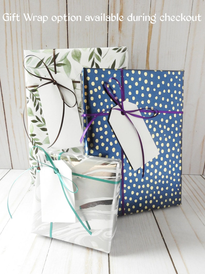 May include: Three gift boxes wrapped in different patterns. The first box is wrapped in white paper with a green leafy design and a brown ribbon. The second box is wrapped in blue paper with white polka dots and a purple ribbon. The third box is wrapped in silver paper with a white swirl design and a teal ribbon. Each box has a white gift tag attached.