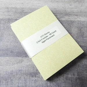 May include: A stack of 60 blank ATC cards in a pale yellow color. The cards are 2.5 x 3.5 inches and are made of aged parchment paper. The cards are wrapped in a white band with the text "ATC Blanks 2.5x3.5 Inches - 60 Count Aged Parchment".