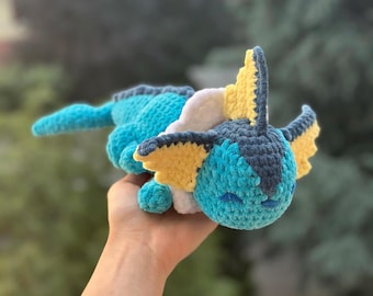 Puede incluir: Un peluche de Vaporeon hecho a mano con ganchillo. El peluche es principalmente turquesa, con detalles amarillos, blancos y azul marino. Tiene una cara sonriente y se sostiene en una mano. Es un juguete tierno.