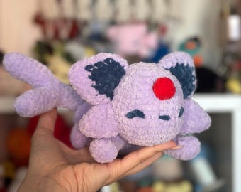 Puede incluir: Un peluche de Espeon hecho a mano, de color lavanda, un personaje de la franquicia Pokémon. El peluche tiene detalles en azul oscuro en las orejas y una gema roja en la frente. Un juguete suave y tierno para los fans.