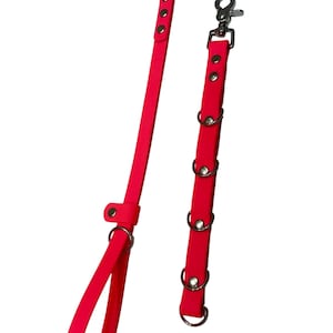 May include: Two bright pink straps with silver-coloured metal hardware. One strap has a loop at the end, and the other has multiple metal rings. Both straps have snap hooks and rivets.
