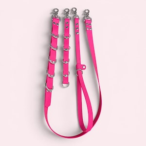 May include: A set of three bright pink straps featuring silver-toned metal hardware. The straps include multiple D-rings, swivel snap hooks, and rivets. The design consists of two shorter, multi-ring segments and one longer, adjustable strap with a loop.