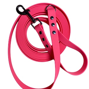 May include: A vibrant pink dog lead with a silver metal clasp and rivets. The lead is coiled and has a textured surface. The handle is a loop, designed for pet owners.