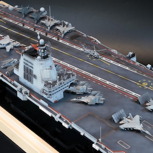 May include: Detailed model of an aircraft carrier with miniature airplanes and helicopters on the deck. The carrier is gray with red and yellow markings, and a tower structure. A scale model for collectors.