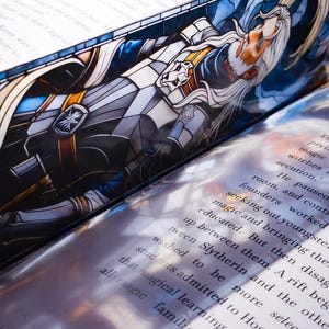 May include: A bookmark with a stained-glass design depicting a wizard with long white hair and a beard. The bookmark is placed within the pages of a book, with printed text visible.