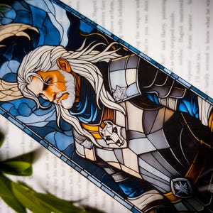 May include: A stained glass bookmark featuring a white-haired man with a beard, wearing a blue and silver armor with a wolf symbol. The background is a blue and white stained glass design.