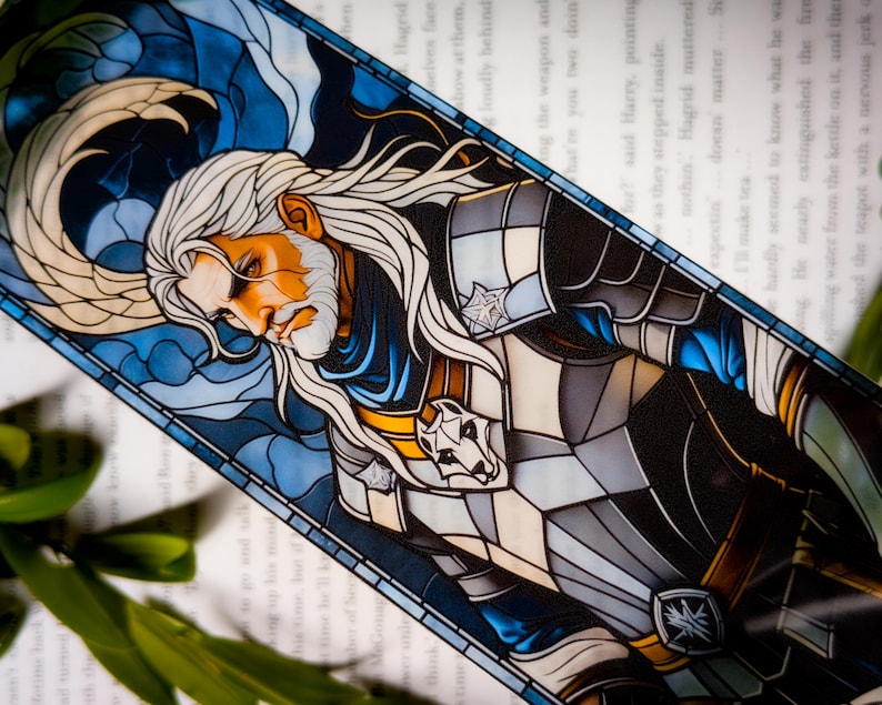 May include: A stained glass bookmark depicting a character with long white hair and a beard in armour, with a wolf emblem. The design is set against a blue and white background. The bookmark is rectangular in shape.