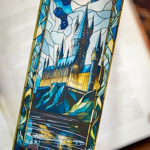 May include: A stained glass bookmark featuring a blue and yellow depiction of Hogwarts castle, a fictional school of witchcraft and wizardry, against a night sky with a full moon.