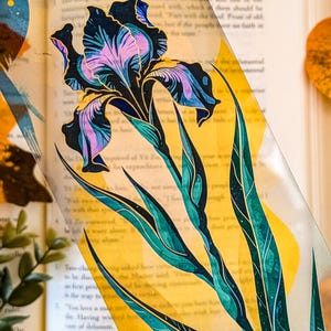 May include: A transparent rectangular bookmark featuring a detailed illustration of a purple and blue iris flower with green stems and leaves, set against a vibrant yellow background with abstract blue and gold accents and fine line details.