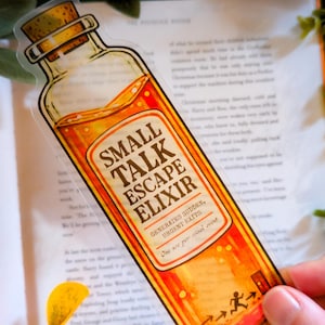 Puede incluir: Un marcapáginas transparente con forma de botella de poción con el texto "SMALL TALK ESCAPE ELIXIR". La botella contiene un líquido naranja y tiene un tapón de corcho. Diseñado para salidas urgentes de eventos sociales.