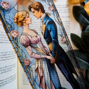May include: A bookmark featuring a romantic illustration of a couple in period clothing, set against a stained-glass window design with pink roses. The man wears a blue coat, and the woman wears a pink dress.