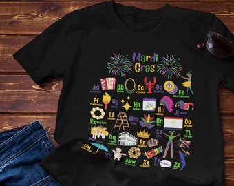 May include: Black t-shirt with a Mardi Gras alphabet design. The letters are illustrated with images of Mardi Gras traditions, such as beads, masks, and king cakes. The text "Mardi Gras" is at the top of the design.