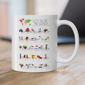 Pode incluir: Caneca de cerâmica branca com um mapa mundial colorido e o texto "Let's go see the world" impresso nela. O mapa mostra as bandeiras de diferentes países organizadas alfabeticamente.