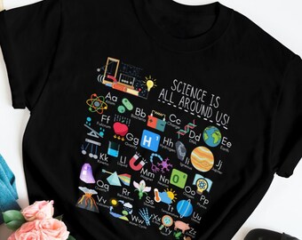 May include: Black t-shirt with a white graphic of a science alphabet with colorful illustrations. The text on the shirt reads "Science is all around us!"