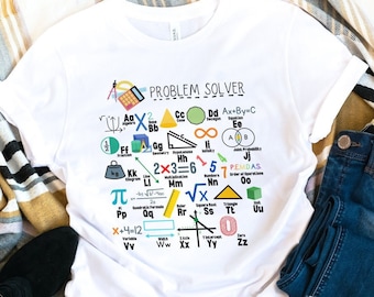 Könnte beinhalten: Weißes T-Shirt mit einer Grafik von mathematischen Symbolen und dem Text "Problem Solver". Das Shirt wird auf einem weißen Hintergrund mit einer gestreiften Decke, blauen Jeans und schwarzen Stiefeletten gezeigt.