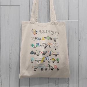 May include: A white canvas tote bag with the text "PROBLEM SOLVER" printed on it. The bag is decorated with colourful mathematical symbols and equations.