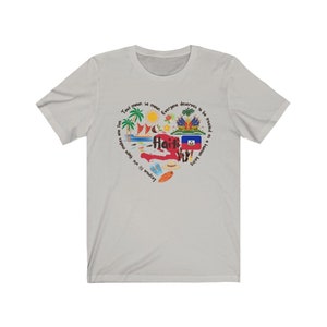May include: A light gray t-shirt with a graphic design of a heart-shaped outline of Haiti. The design includes the Haitian flag, palm trees, a sun, a surfboard, and the text "Tout moun se moun. Everyone deserves to be treated as a human being. Lesowe f&egrave; viv. Hare makes an e."
