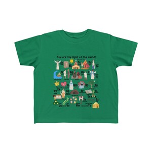 May include: A green t-shirt with a colorful alphabet design featuring illustrations of religious figures and objects. The text "You are the light of the world!" is printed at the top of the shirt.