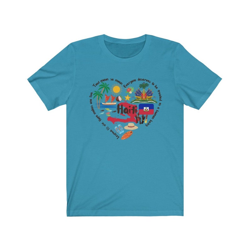 May include: A turquoise blue t-shirt with a circular design featuring the outline of Haiti, the Haitian flag, and various icons representing the country. The text "Tout moun se menm" and "Everyone deserves to be treated as a human being" are written around the design.