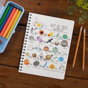 May include: A white spiral bound notebook with the words "OUT OF THIS WORLD!" on the cover. The cover features an alphabet chart with illustrations of space-related objects and terms, such as a rocket, a comet, a galaxy, and a telescope.