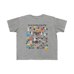 May include: A gray t-shirt with a colorful alphabet design featuring illustrations of biblical figures and scenes. The text "You are the light of the world! Matthew 5:14" is printed on the shirt.