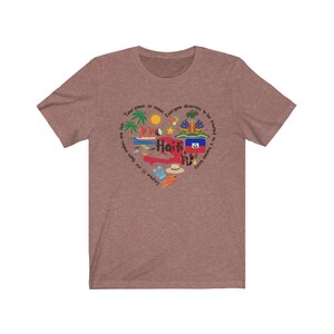 May include: A heather brown t-shirt with a heart-shaped design featuring the word "Haiti" and various symbols representing the country, including a palm tree, a coconut, a boat, and the Haitian flag. The text around the heart reads "Tout moun se moun, everyone deserves to be treated as a human being".