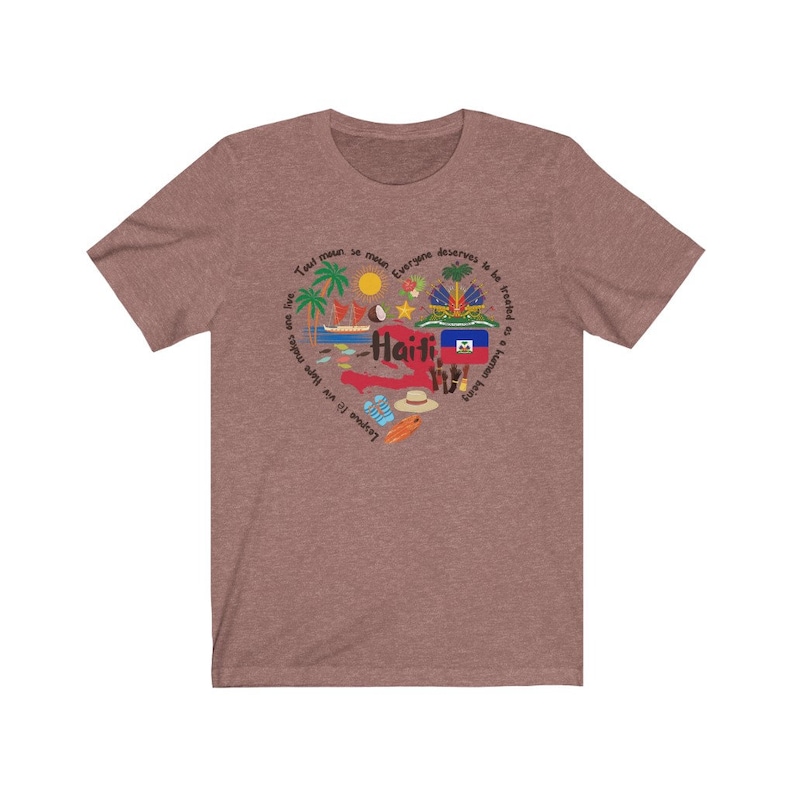 May include: A heather brown t-shirt with a heart-shaped design featuring the word "Haiti" and various symbols representing the country, including a palm tree, a coconut, a boat, and the Haitian flag. The text around the heart reads "Tout moun se moun, everyone deserves to be treated as a human being".