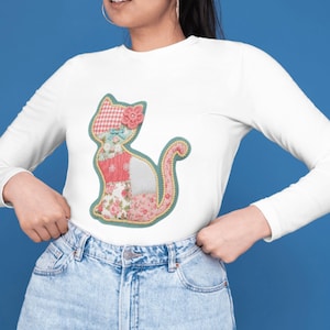 Op de afbeelding: Wit shirt met lange mouwen met een patchwork kattenontwerp. De kat is gemaakt van bloemen- en stoffen met patronen in roze, rood en blauw, met een roze bloem op het hoofd. De kat is omlijnd in een lichtgroene kleur.