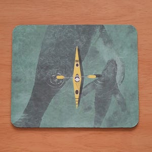 May include: A rectangular coaster depicting a yellow kayak with a person inside, paddling on a green water surface. The design includes a silhouette of a person's arms and hands, with ripples around the kayak.