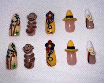 May include: A collection of ten artificial nails with various designs. The designs include floral patterns, monkey figures, yellow hats with black bands, and nails with fruit slices. The nails are in various colors, including beige, yellow, pink, and brown.