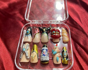 May include: A clear plastic case with 10 false fingernails. The nails are decorated with various designs, including a snake, a cowboy boot, a bull's head, and a turquoise stone. The text "COWBOY CARTER" is visible on one of the nails.