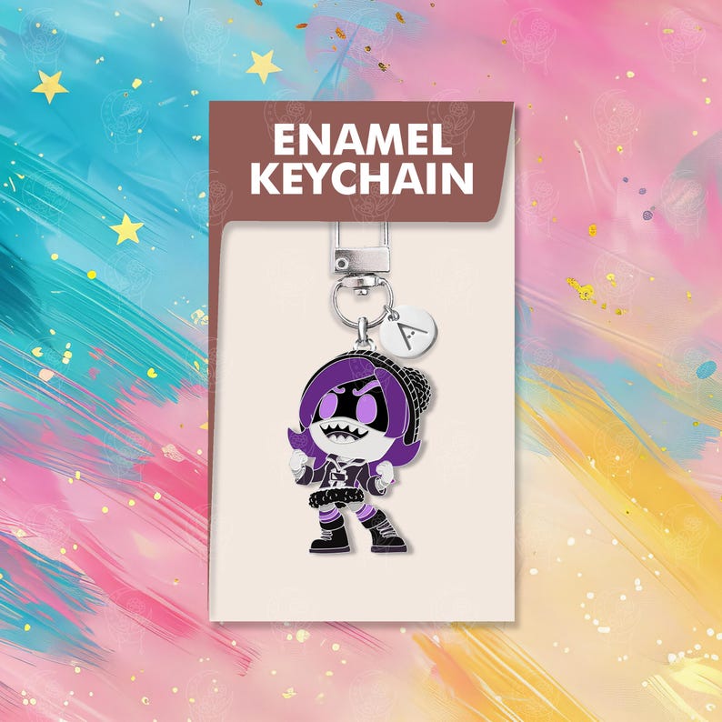 以下が含まれることがあります： 紫色の髪と黒い衣装の漫画のキャラクターが特徴の、エナメルキーホルダー。キーホルダーにはシルバーの留め金と、文字「A」の小さなチャームが付いています。パッケージには「ENAMEL KEYCHAIN」と書かれています。