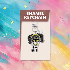以下が含まれることがあります： 黒い髪と黄色のアクセントを持つ漫画のキャラクターが特徴の、エナメルキーホルダー。キーホルダーはシルバーの留め金と小さなチャームに付いています。カードには「ENAMEL KEYCHAIN」と書かれています。