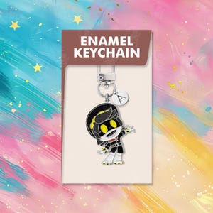 以下が含まれることがあります： 黒、白、黄色の漫画のキャラクターが描かれたエナメルキーホルダー。キーホルダーにはシルバーの留め金と、文字「A」の小さなチャームが付いています。パッケージには、茶色の背景に白い文字で「ENAMEL KEYCHAIN」と書かれています。