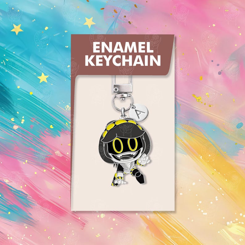 以下が含まれることがあります： 黒と黄色の配色のアニメキャラクターが特徴的なエナメルキーチェーン。キーチェーンはシルバーの留め金と、文字「A」の小さなチャームが付いています。パッケージには「ENAMEL KEYCHAIN」と書かれています。