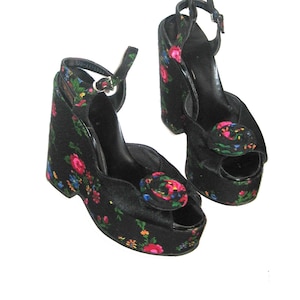 Op de afbeelding: Een paar zwarte platform sandalen met een bloemenprint. De sandalen hebben een peeptoe en een enkelband.