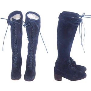 May include: A pair of dark blue suede knee-high boots with lace-up fronts. The boots have a block heel and are tied with long laces.