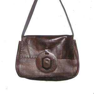 May include: A brown leather shoulder bag with a circular detail on the front. The bag has a flap closure and a single strap.