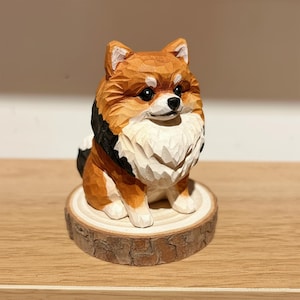 May include: A hand-carved wooden dog figurine, featuring a fluffy, detailed design. The dog has brown, white, and black fur, with a small black nose and eyes. It sits on a small, round wooden base, showcasing the natural wood grain.