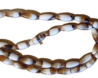 May include: A strand of oval-shaped beads in shades of brown and white. The beads are strung together, forming a necklace or bracelet. The beads have a polished, glossy finish, and the overall design is simple and elegant.