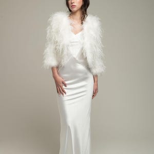 Könnte beinhalten: Eine weiße Feder-Brautbolero-Jacke mit langem Ärmel. Die Jacke ist aus weichen, flauschigen Federn gefertigt und hat einen zarten, femininen Look.