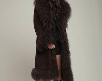 May include: A long, dark brown coat with a faux fur collar, cuffs, and trim. The coat is worn with black boots and sunglasses. The coat's length extends to the ankles.
