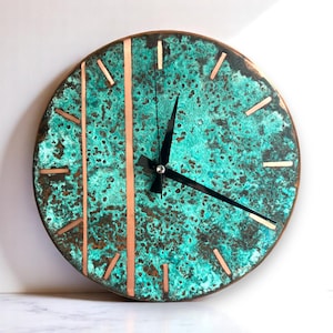 May include: Round wall clock with a turquoise and copper finish. The clock face has a textured appearance with copper accents and black clock hands. The clock's design features vertical copper stripes and copper-colored markers for the hours.