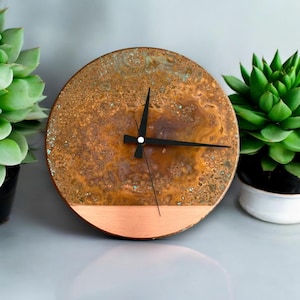 May include: A round copper clock with a black face and hands. The clock has a copper band around the edge and a copper base.