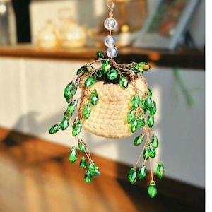 May include: A hanging decorative plant with a woven basket and cascading green crystal leaves. The plant is suspended by a copper wire chain with clear and blue glass beads. The plant is a unique home decor item.