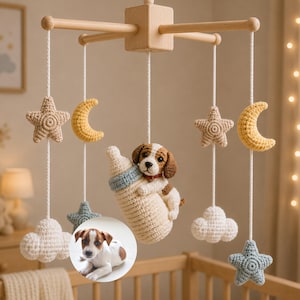 Puede incluir: Un m&oacute;vil de cuna con estructura de madera clara y cuerdas blancas que sostienen figuras de ganchillo: dos estrellas beige, dos lunas crecientes amarillas, dos nubes blancas, dos estrellas azules y un cachorro abrazando un biber&oacute;n.