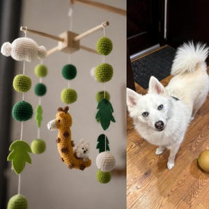 Puede incluir: Un m&oacute;vil colgante con marco de madera del que cuelgan esferas de ganchillo en tonos verdes y blancos, hojas de fieltro y una figura de jirafa de ganchillo con un peque&ntilde;o perro blanco sobre su lomo, junto a un perro blanco.