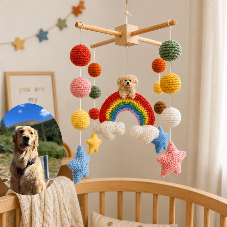 Puede incluir: Un m&oacute;vil colgante para cuna con marco de madera en cruz y elementos tejidos a ganchillo que incluyen esferas de colores, estrellas, nubes, un arco&iacute;ris y una peque&ntilde;a figura de perro. Un recuadro circular muestra un golden retriever al aire libre.