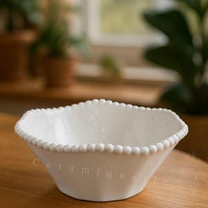 Puede incluir: Un cuenco de cerámica blanco con borde de cuentas. El cuenco tiene forma hexagonal y está sobre una superficie de madera. La palabra "Ceramique" está impresa en el lateral del cuenco.